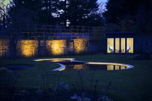 Garden Lighting - garden lit up at dusk, shaped pond with perimeter lighting, stone wall with feature lighting, modern summerhouse with interior lighting